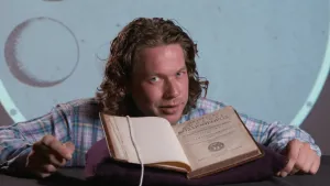 Een foto van presentator Pascal. Hij zit achter een tafel. Voor hem ligt een heel oud opengeslagen boek van de wetenschapper Christiaan Huygens. Pascal kijkt in de camera.