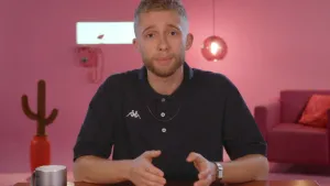 Een foto van presentator Jard in een roze studio. Hij kijkt in de camera en legt iets uit. Op de achtergrond zie een roze telefoon, lamp, cactus en een roze bank.