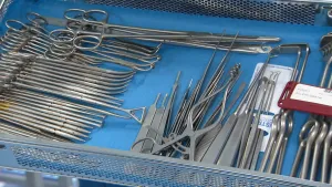 Een foto van een stalen mandje met een blauwe ondergrond waar medische instrumenten van staal inliggen: scharen, pincetten, tangen en haakjes zijn te zien. De instrumenten liggen klaar om schoongemaakt te gaan worden.