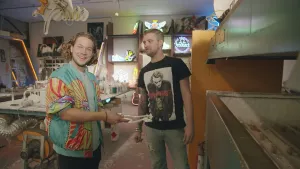 Een foto van presentator Pascal. Hij is op bezoek bij neonglasblazer Djahvy in zijn werkplaats. Pascal houdt een glazen buis vast. Die buis heeft allerlei bochten. 