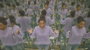 Een foto van presentator Sosha die een hokje staat van drie spiegels. Door de spiegels is haar spiegelbeeld erg vaak te zien, zowel naast haar als achter haar.