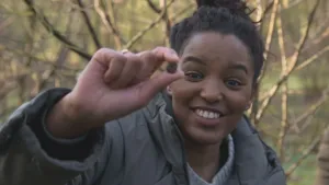 Een foto van presentator Sosha die een truffel laat zien die ze tussen haar vingers heeft. Op de achtergrond is er bos te zien.