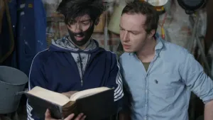 Een foto van Pieter en Willem in hun werkplaats. Ze kijken in een dik boek dat Willem vast houdt. Willem heeft allemaal zwart spul op zijn gezicht; het lijkt wel roet.