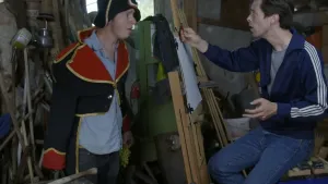 Een foto van presentatoren Willem en Pieter. Pieter staat in een kostuum en Willem heeft een potlood in zijn hand en zit achter een vel met papier waarop hij Pieter gaat na tekenen.
