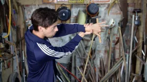 Een foto van presentator Willem in een werkplaats. Hij doet een goocheltruc met een hamer. Het lijkt net alsof de hamer achter zijn hand zweeft. 