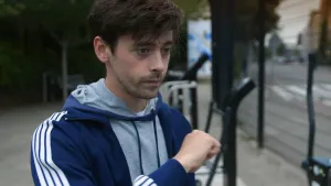 Een foto van presentator Willem. Hij staat buiten en heeft een trainingsjack met capuchon aan. Hij houdt een gebalde vuist voor zijn borst en kijkt dromerig.