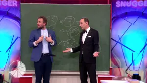 Een foto van twee mannen die naar links kijken en voor een schoolbord staan. Op het schoolbord staan in krijt drie deels zichtbare rekensommen. De ene man wijst met zijn handen naar zijn borst, de andere heeft zijn handpalmen omhoog naast zijn lichaam.