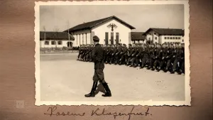 Een foto van een oude zwartwit-foto die op een tafel ligt. Hierop zie je op de voorgrond een militair die naar een groep marcherende militairen op de achtergrond kijkt. Daarachter zie je witte gebouwen met daarop een beeld van een adelaar.