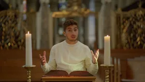 Een foto van presentator Nizar die in de kerk tussen twee kaarsen in achter een tafel staat waar een Bijbel op ligt.