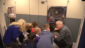 Een foto waar een man aan een groep kinderen een crematie oven laat zien.
