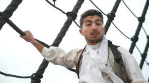 Een foto van presentator Nizar die een onderdeel van een mast van een oud zeilschip vasthoudt.