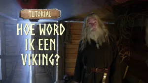 Een foto van een man in een schuur met een bruin pak, een baard met vlechtjes erin en een bruine riem om met een goudkleurige schede eraan om een dolk, een soort mes, in te doen. Links naast de man is te lezen: "Tutorial - Hoe Word ik een Viking?".