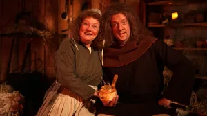 Een foto van een vrouw en een man in Middeleeuwse kleren. Ze zijn in een Middeleeuwse woning en de man houdt een pijp met tabak in zijn hand. Ze kijken in de camera.