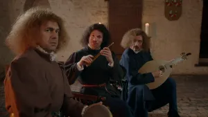 Een foto van drie mannen, minnezangers, in middeleeuwse kleding, bruin, zwart en blauw van kleur. De voorste man heeft een trommel vast, de middelste man een ronde, bruine fluit en de rechterman een lichtbruine luit, een middeleeuwse gitaar. 