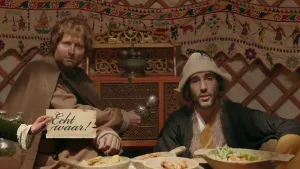 Een foto in een joert, een ronde, cirkelvormige tent, waarin mensen in Mongolië wonen. Eén man met een bruine microfoon interviewt een als Dzjengis Khan verklede man in zwart pak en lichtbruine hoed. Ervoor heeft een hand een bord met "Echt waar!" vast.