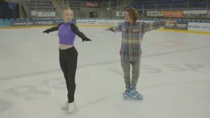 Een foto van de zestienjarige kunstschaatser Lindsay van Zundert. Ze staat samen met de presentator binnen in een hal op het ijs. Ze hebben schaatsen aan en staan in dezelfde houding, met hun armen gestrekt opzij.