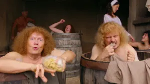 Een foto van vier mensen die in hun eentje naakt in een ronde, houten ton zitten en zich wassen in niet-zichtbaar water. Eén persoon heeft een lichtgele spons vast met wit schuim erop, een ander bijt in een lichtbruine doek die op de rand van de ton ligt.