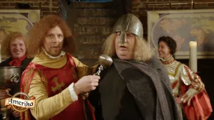 Een foto van een man in een rode cape met twee goudkleurige kruizen erop en een metalen ding als microfoon. Hij interviewt een man verkleed als Leif Eriksson in zwart pak, met grijze cape en met metalen helm. Linksonder staat "Amerika" in een scheepswiel.