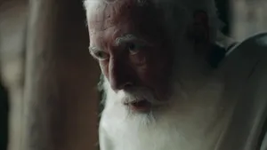 Een foto van een oude man met een witte baard. Hij zit aan de rechterkant en kijkt naar links.