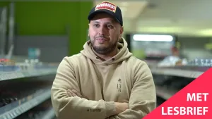 Een foto van een loodgieter die met zijn armen over elkaar tussen de schappen staat van een winkel.