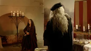 Een foto van een man verkleed als schilder Leonardo da Vinci en een vrouw verkleed als de Mona Lisa op een stoel of kruk in de achtergrond. De schilder is bezig op een doek zijn bekende portret de Mona Lisa te schilderen en de vrouw poseert.