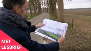 Een foto van een man op een weg, op het platteland. Hij kijkt naar een plaatje dat hij in zijn handen houdt. Daarop zie je een asfaltweg, gras en een gebouw. Linksonder in beeld staat de tekst 'Met lesbrief'.