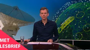 Een foto van een presentator die in de studio voor de camera zit. Op de achtergrond is er aan de linkerkant een grote satelliet schotel te zien en rechts heel veel cirkels en punten op een soort bol.