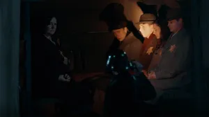 Een foto van vijf Joodse mensen met een gele jodenster op hun borst, die achterin een vrachtauto zitten in het donker. Een Nazi, een Duitse soldaat met een donkerkleurig pak en een helm op, schijnt met een zaklamp in het gezicht van één van de mensen.