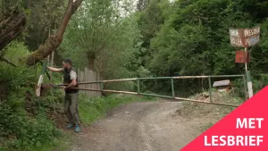 Een foto van een man die bezig is met een gesloten hek op een zandpad door een dicht bos.