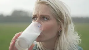 Een foto van presentator Janouk die op een weiland melk drinkt wat gemaakt is van planten.