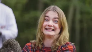 Een foto van presentator Emma die ongemakkelijk en nerveus in de camera kijkt. Linksonder in beeld is een egel te zien en daarachter een witte doktersjas. 