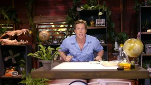 Een foto van bioloog Freek Vonk. Hij zit achter een houten bureau en kijkt in de camera. Op het bureau staat een plant en een wereldbol. Op een kast staat de schedel van een krokodil. Verder zijn er nog meer kasten met allerlei spullen te zien.