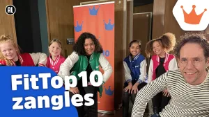 Een foto een man en 5 meisjes die op krukken zitten en naar de camera kijken. Achter hen hangt een oranje doek met blauwe kroontjes erop. Linksonder op de foto staat de tekst "FitTop10 zangles". 