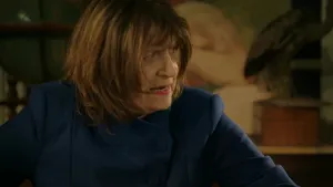 Een foto van een vrouw met donkerblauwe kleren aan. Ze kijkt ernstig naar iemand die buiten beeld is. Ze praat tegen die persoon. 