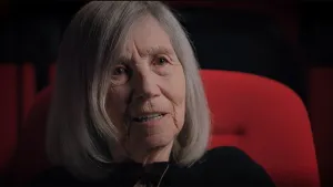 Een foto een bejaarde vrouw die voor de camera zit te praten.