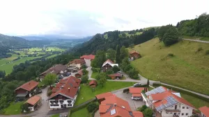 Een foto van een bergachtig gebied met huizen. De meeste huizen zijn wit met een rood dak. Tussen de huizen zijn wegen en parkeerplaatsen. Rondom en op de achtergrond zijn veel bomen en weilanden te zien.