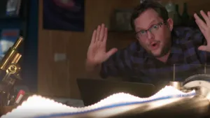 Een foto van Diederik Jekel in een kamer. Op de voorgrond zie je een golf uitgebeeld met lampjes. Ook zie je een microscoop. Diederik doet zijn handen omhoog. Hij is erg onder de indruk van iets.