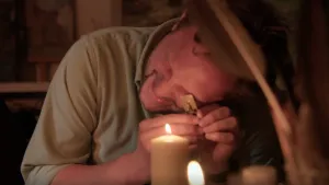 Een foto van presentator Diederik Jekel die met een oog door een gaatje kijkt van een plaatje van metaal naar een vlam van een kaars.