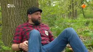 Een foto van presentator Tim die in het bos met zijn rug tegen een boom aan zit.