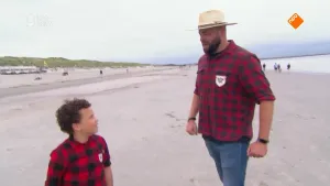 Een foto van boswachter Tim die samen met een jongetje op het strand staat in Zeeland. Op de achtergrond zijn er nog meer mensen te zien die over het strand lopen.