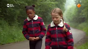 Een foto van twee meisjes die langs in weg lopen die door een bos loopt.