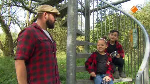 Een foto van boswachter Tim die tegenover twee kinderen staat die buiten op een trap zitten. Op de achtergrond is er bos te zien.