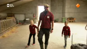 Een foto van presentator boswachter Tim die met twee kinderen door een stal loopt.