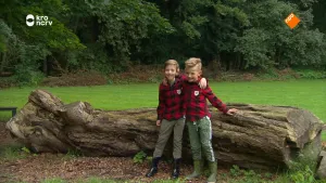 Een foto van twee jongens die tegen een dode boomstam leunen die achter hun op de grond ligt. 