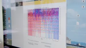 Een foto van een beeldscherm met een grafiek erop. Boven de grafiek staat "Live seismogram" en er zijn blauwe en rode golvende lijnen te zien, die ook over elkaar heenlopen. Een seismoloog meet hiermee aardbevingen door de trilling van de aarde te meten.
