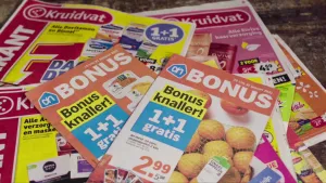 Een foto van folders van Albert Heijn en Kruidvat waar 1+1 gratis aanbiedingen op staan.