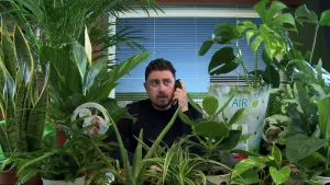 Een foto van een presentator die aan de telefoon zit tussen heel veel kamerplanten.