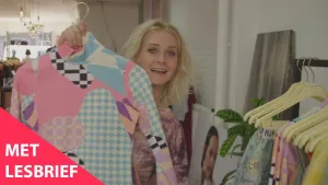 Een foto van presentator Janouk in een kledingzaak. Ze kijkt in de camera en toont de kijker een kleurrijk truitje. Dat truitje bestaat uit allemaal verschillende patronen. Linksonder in beeld staat de tekst "Met lesbrief".