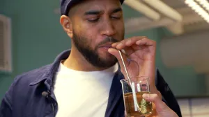 Een foto van Edson die in een glazen maatbeker, waar streepjes en maten op de zijkant staan, blaast. Hij blaast door een stalen rietje. In de maatbeker zit urine of plas van Tim. Dit is een experiment of ze drinkwater kunnen maken van hun eigen plas.