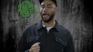 Een foto van Edson die zijn ogen dicht heeft. Ook heeft hij zijn mond open, omdat hij een boer laat. Links naast zijn mond is een getekend groen wolkje te zien. Edson draagt een blauwgrijze blouse en pet. De achtergrond is grijs met zwart.